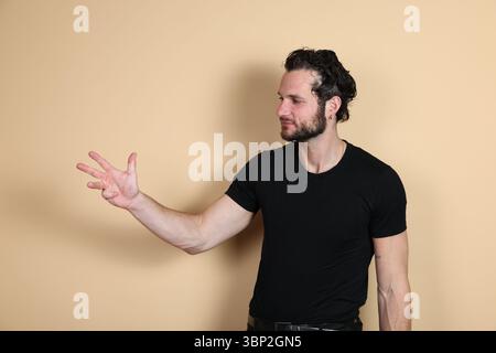A young man in a black t-shirt displays four fingers on his hand while looking towards his hand or aside, indicating the number four or counting. Stud Stock Photo