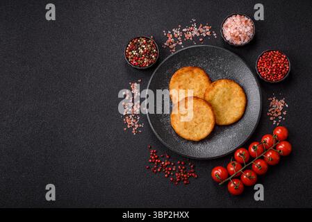 Hash browns, a breakfast food made of potatoes, onions and vegetables. Hash browns with potatoes, salt and spices on a dark concrete background Stock Photo