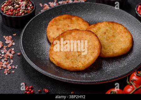 Hash browns, a breakfast food made of potatoes, onions and vegetables. Hash browns with potatoes, salt and spices on a dark concrete background Stock Photo