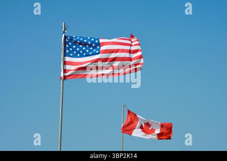 The American flag and Canadian flag fly together against a clear blue sky. Stock Photo