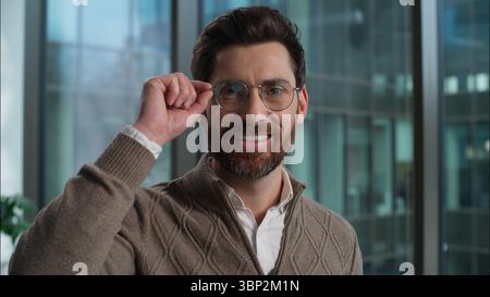 Caucasian man adult male wearing eyeglasses holding glasses guy successful businessman smiling business portrait in office manager employee looking at Stock Photo