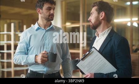 Caucasian men businessmen business partners friendly conversation dialogue talking in office coffee break drinking together guys male co-workers Stock Photo