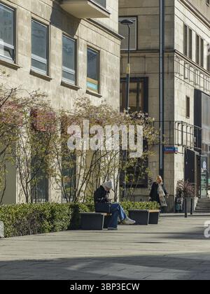 Young woman wearing winter hat and jacket sitting on bench and using smartphone, city, Warsaw, Poland, Europe Stock Photo