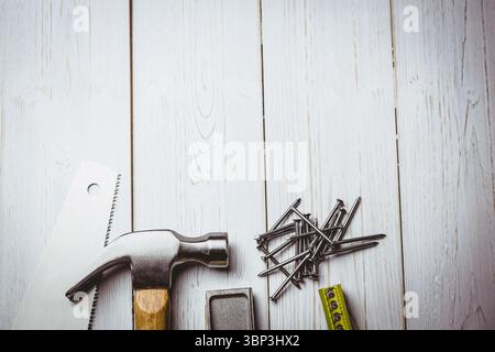 Flat illustration showing claw hammer with wooden handle beside hand saw, nails, tape, copy space Stock Photo