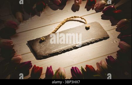 Flat design is showing rough slate sign with rope handle on whitewashed plank, tulip blossom ring Stock Photo