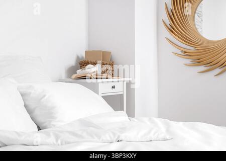 Comfortable bed, table with books and headphones in light bedroom Stock Photo