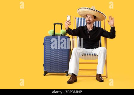 Young businessman with sombrero hat taking selfie in deck chair on yellow background. Summer vacation concept Stock Photo