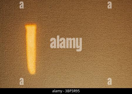 Single vertical orange light streak illuminates textured wall, creating striking contrast on muted background and embodying simplicity in expression. Stock Photo