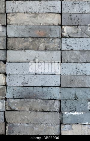Stacked gray rectangular concrete bricks create detailed geometric pattern. Varying in shades and textures, weathered blocks form industrial scene. Stock Photo