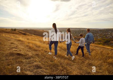 Back view of family holding hands and walking on field during sunset, spending free time outdoors Stock Photo