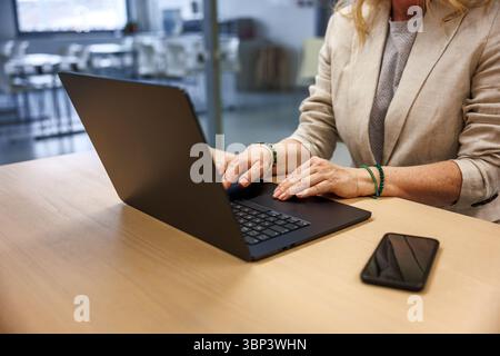Woman entrepreneur typing on laptop while working at office desk, mobile phone within reach. Stock Photo