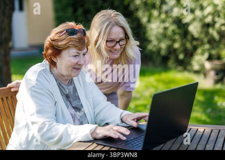 Two smiling mature and senior women are using laptop outdoors. Happy multi-generation family with notebook computer Stock Photo