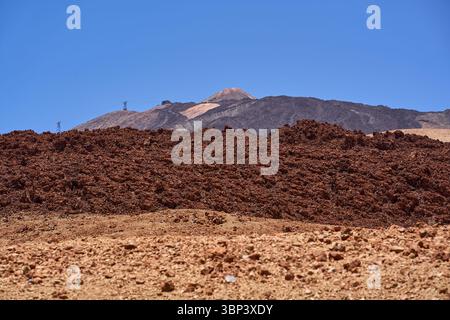 Mount Teide summit and cablecar station seen behind jagged dark lava fields under a clear summer sky Stock Photo