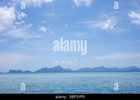 A peaceful seascape capturing the gentle gradation of blues from the clear ocean to the expansive sky, with silhouettes of distant tropical islands Stock Photo