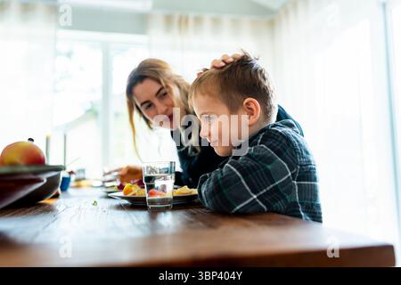 Mother caressing son eating lunch at dining table Stock Photo