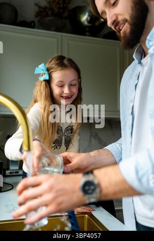 Happy girl with father washing dishes in kitchen sink at home Stock Photo