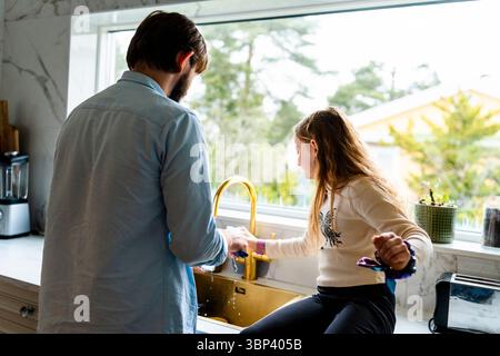 Daughter helping father while washing dishes in kitchen at home Stock Photo
