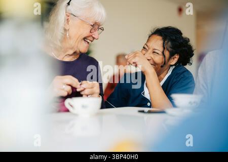 Happy female nurse enjoying leisure time with elderly woman at retirement home Stock Photo