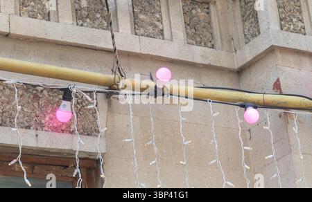 Pink light bulbs on the wall of an old building, white string lights hanging from yellow pipes. Stock Photo