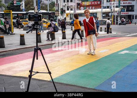 A young woman poses for a selfie at Rainbow Six, the famous rainbow crosswalk in the Ximending Walking District, Taipei, Taiwan Stock Photo