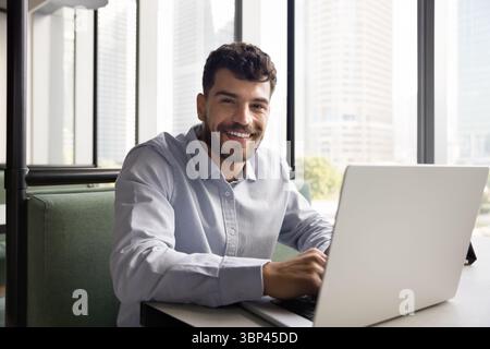 Happy millennial male using notebook at cafe looking at camera Stock Photo