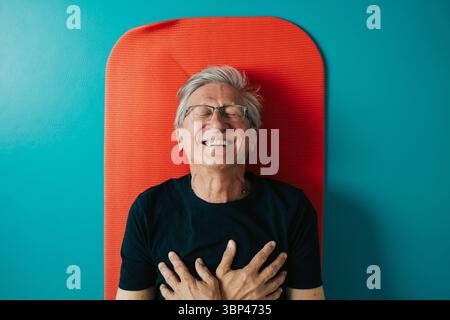 Directly above shot of happy man with hands on chest lying on exercise mat Stock Photo