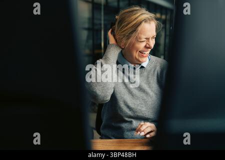 Happy senior businesswoman laughing while sitting at desk in office Stock Photo