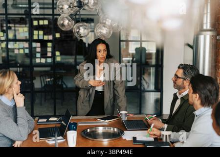 Businesswoman sharing ideas with colleagues sitting around table in meeting Stock Photo