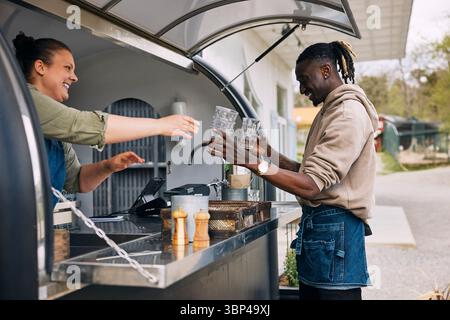 Smiling young man giving stack of glasses to coworker standing in food truck Stock Photo