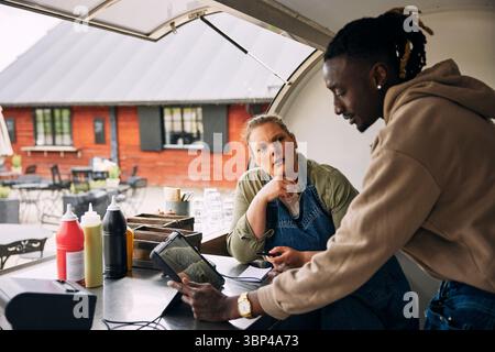 Young woman looking at male friend using tablet PC while bookkeeping in food truck Stock Photo