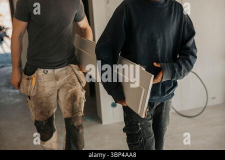 Midsection of male workers carrying wooden planks during home renovation Stock Photo