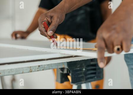 Close-up of male construction worker's hand using tape measure on wooden plank while marking with pencil Stock Photo