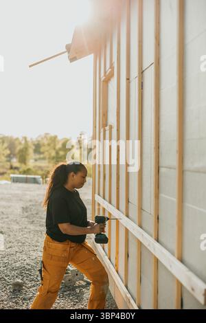 Female worker using drilling wooden plank outside house at sunny day Stock Photo