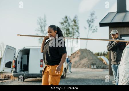 Female and male worker carrying wooden plank outside house Stock Photo
