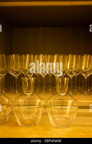 Wine glasses and decanters standing on a wooden shelf in warm light, ready for a celebration or a dinner party Stock Photo