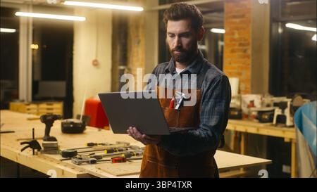 Caucasian wood master man typing laptop shopping app online in workshop builder handyman guy using Internet pc carpenter male buying goods artist Stock Photo