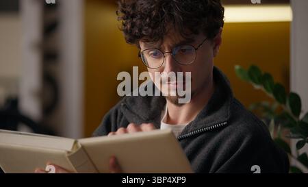 Pensive serious Caucasian hipster guy thinking reading book at home male reader man read classic literature novel pages studying indoors smart learner Stock Photo