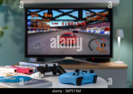Milan, Lombardy, Italy - February 24, 2025: Blue gamepad on table with retro car racing Gran Turismo videogame running on tv screen in living room Stock Photo