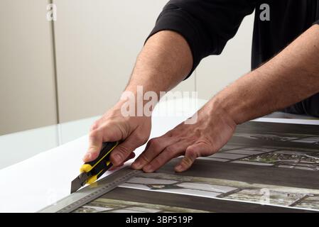 Close up of hands using cutter and metal ruler to cut paper print in a print shop Stock Photo