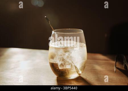 Cool sake served over ice in sunlit glass on wood, stylish simple setting ideal for luxury dining or lifestyle blogs, hospitality, cocktail bar Stock Photo