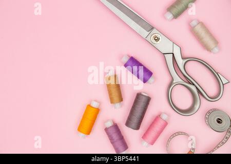 Large tailor scissors, spools of bright thread, and tape on soft pink background, ideal for sewing, crafts, or textile ads, tailoring tools, textile c Stock Photo