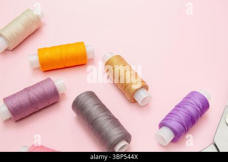 Vivid spools of thread arranged on light pink surface, ideal for tailoring, embroidery or crafting visuals, sewing blog, textile crafting Stock Photo