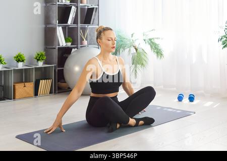 Sporty calm young woman breathig deeply and practicing yoga on fitness mat, keeping eyes closed Stock Photo