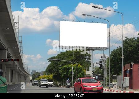 Blank white billboard on roadside with traffic cars and motorcycle under blue sky and clouds background, concept of outdoor advertising marketing sign Stock Photo