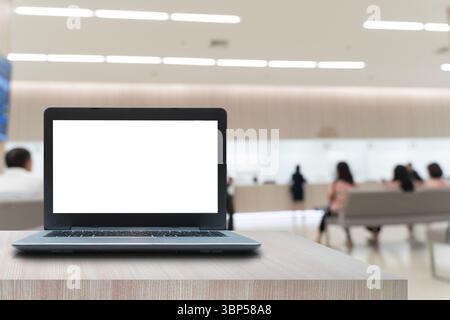 Laptop computer with blank white screen placed on wooden table in modern bright waiting area or lobby, with people sitting and blurred background, con Stock Photo