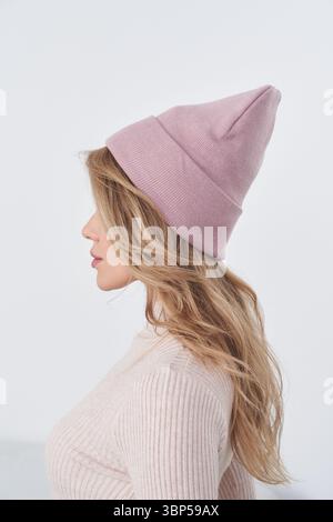 Profile view of a person wearing a pink knit hat and a matching ribbed sweater, with long wavy hair cascading down. The hat's pointed top adds a Stock Photo
