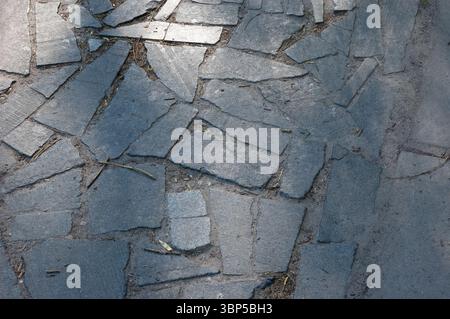Old stone-paved path made of irregular granite slabs. The surface is uneven, with debris between the stones and small depressions from wear and age. Stock Photo