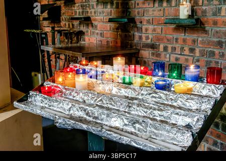 Colorful votive candles burning inside a church, symbolizing prayer, hope, and devotion in a peaceful religious setting. Stock Photo