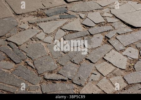 Old stone-paved path made of irregular granite slabs. The surface is uneven, with debris between the stones and small depressions from wear and age. Stock Photo