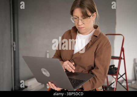 Businesswoman holding laptop while managing home renovation on construction site. small business, smart project leadership, interior repair, and Stock Photo